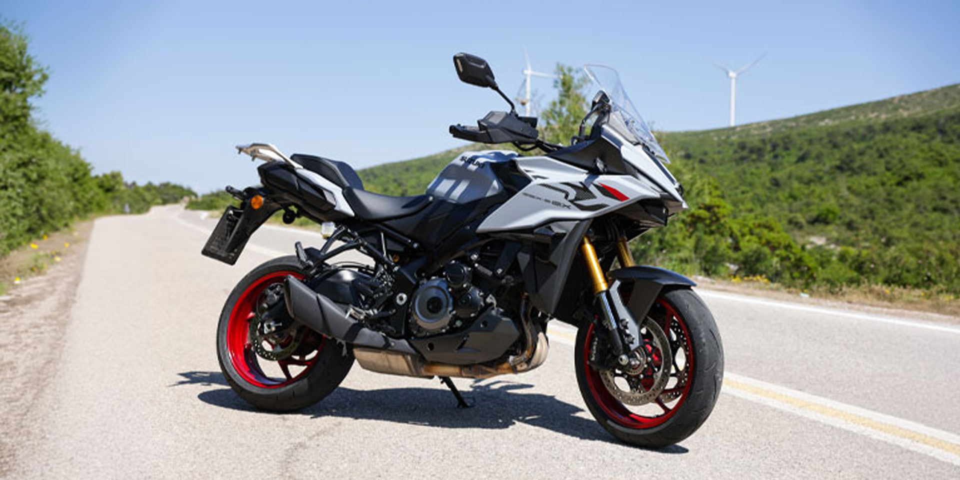 Suzuki GSX-S1000GX 2026 σε γκρι και μαύρο με κόκκινους τροχούς, σταθμευμένη σε ορεινό δρόμο