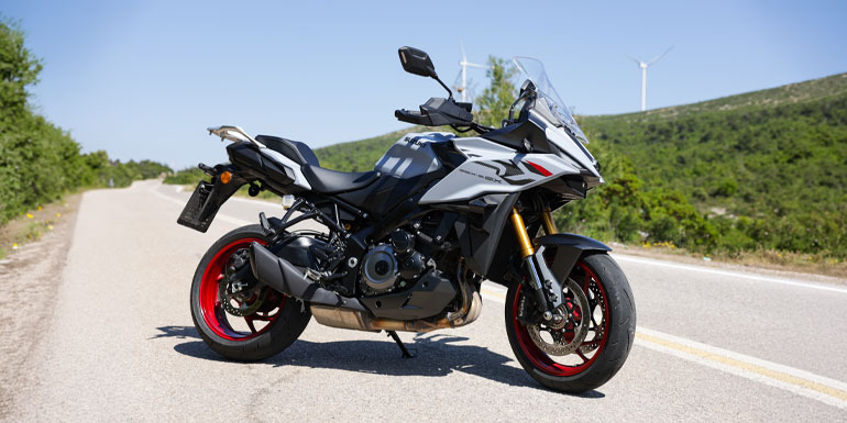 Suzuki GSX-S1000GX 2026 σε γκρι και μαύρο με κόκκινους τροχούς, σταθμευμένη σε ορεινό δρόμο